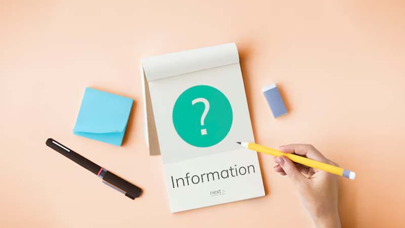 A hand holding a yellow pencil over a notepad with the word "Information" written on it. Above the text, there is a green circle with a white question mark inside. The picture includes a pen, sticky notes, and an eraser.