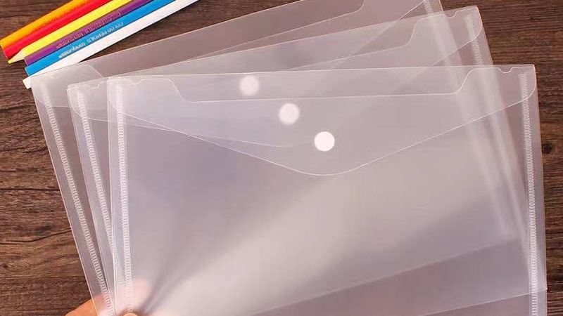 A hand holding three clear plastic envelopes, each slightly fanned out, with different colors of crayon by the sides.