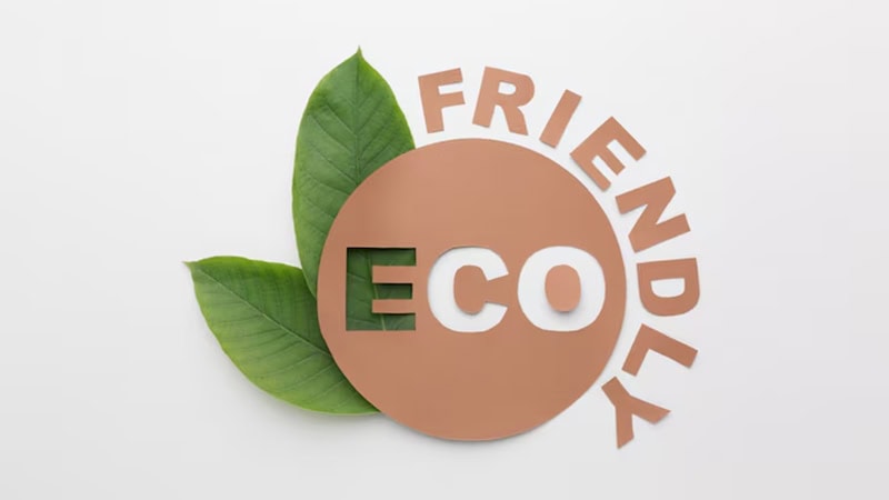 A brown paper cutout says "ECO FRIENDLY" with a circular design. Green leaves peek from behind, symbolizing nature. The white background makes the words and leaves stand out. The design gives a clean and eco-conscious feel, promoting sustainability and environmental care.